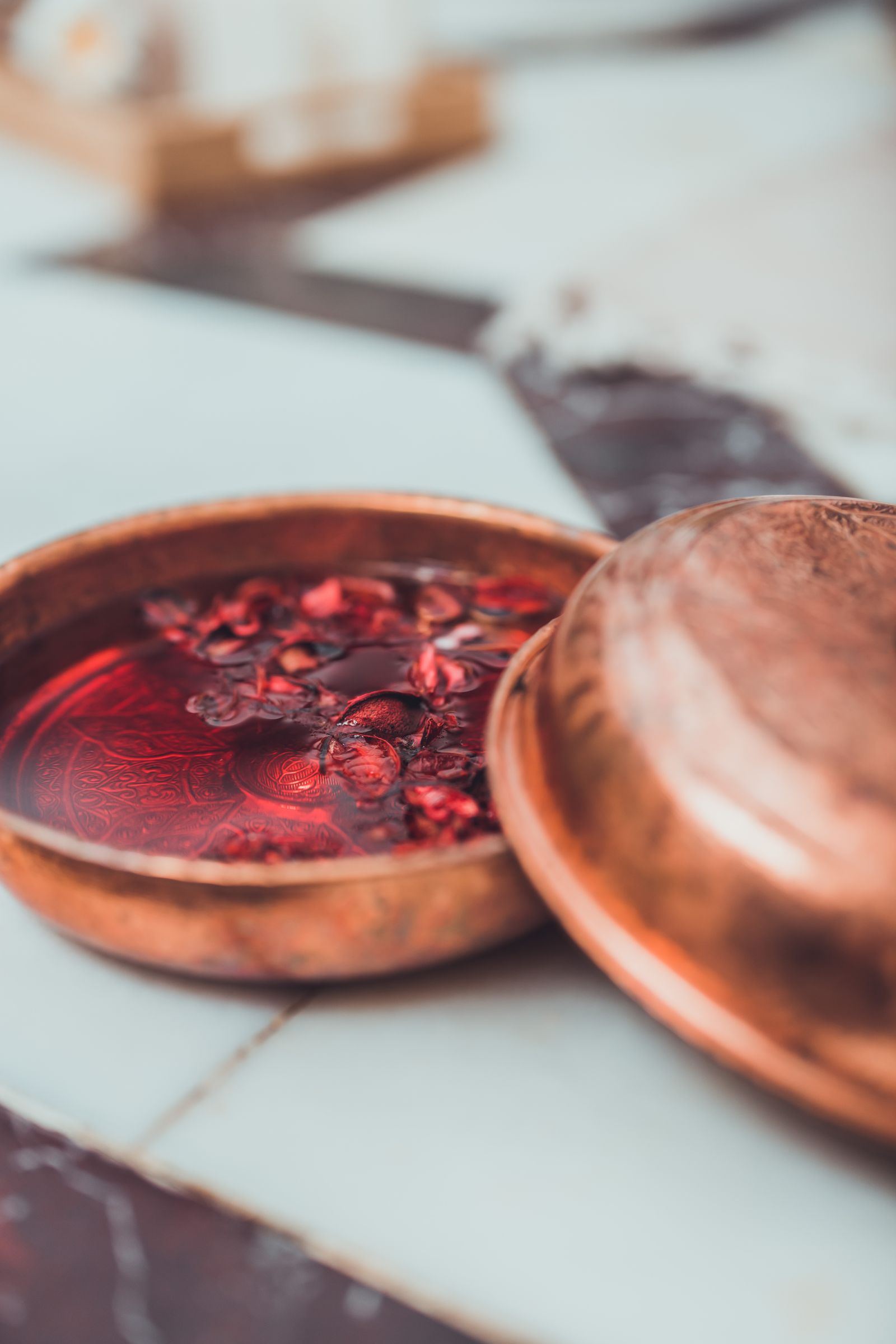 A copper basin filled with a deep red herbal soak and dried botanicals