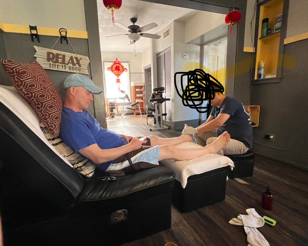 A client reclined in our black chair while we work the feet, RELAX LIFE IS GOOD on the wall