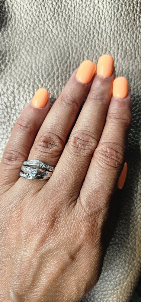 Short glossy orange manicure on a left hand, silver rings on the ring finger.