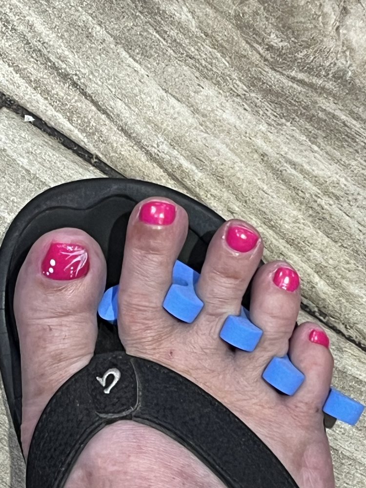 Hot pink pedicure with white floral art on the big toe, blue separators still on.