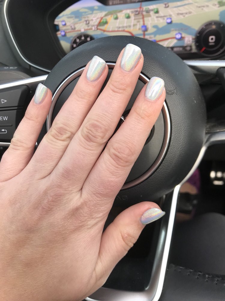 Short holographic silver manicure on a steering wheel.