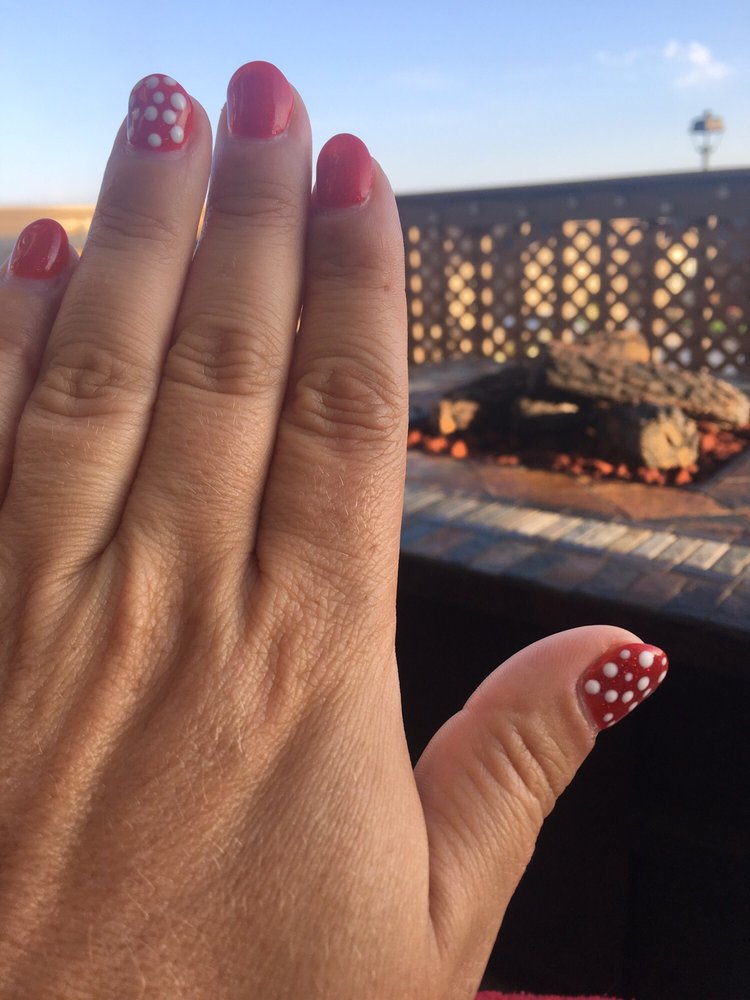 Short red manicure with white polka dots on the thumb and index.
