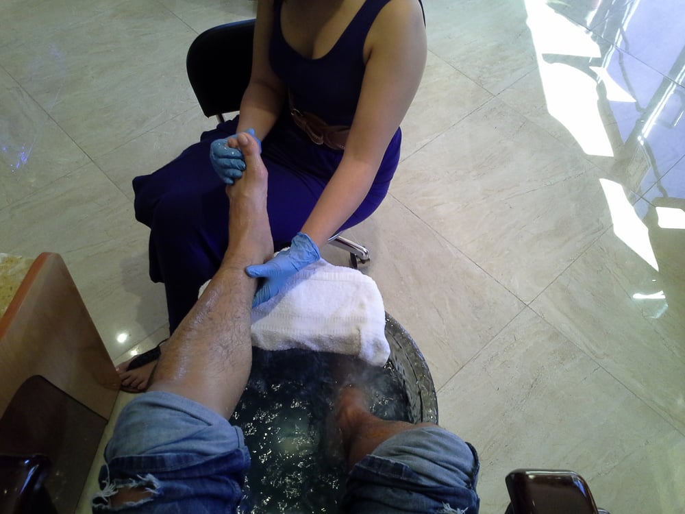 A pedicure in progress: one foot in the spa, a tech in blue gloves working the other on a white towel.