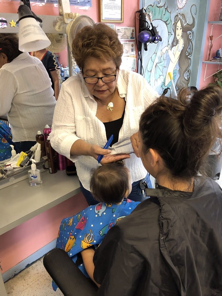 Ada cutting a child's hair in our chair, mermaid wall behind the cape