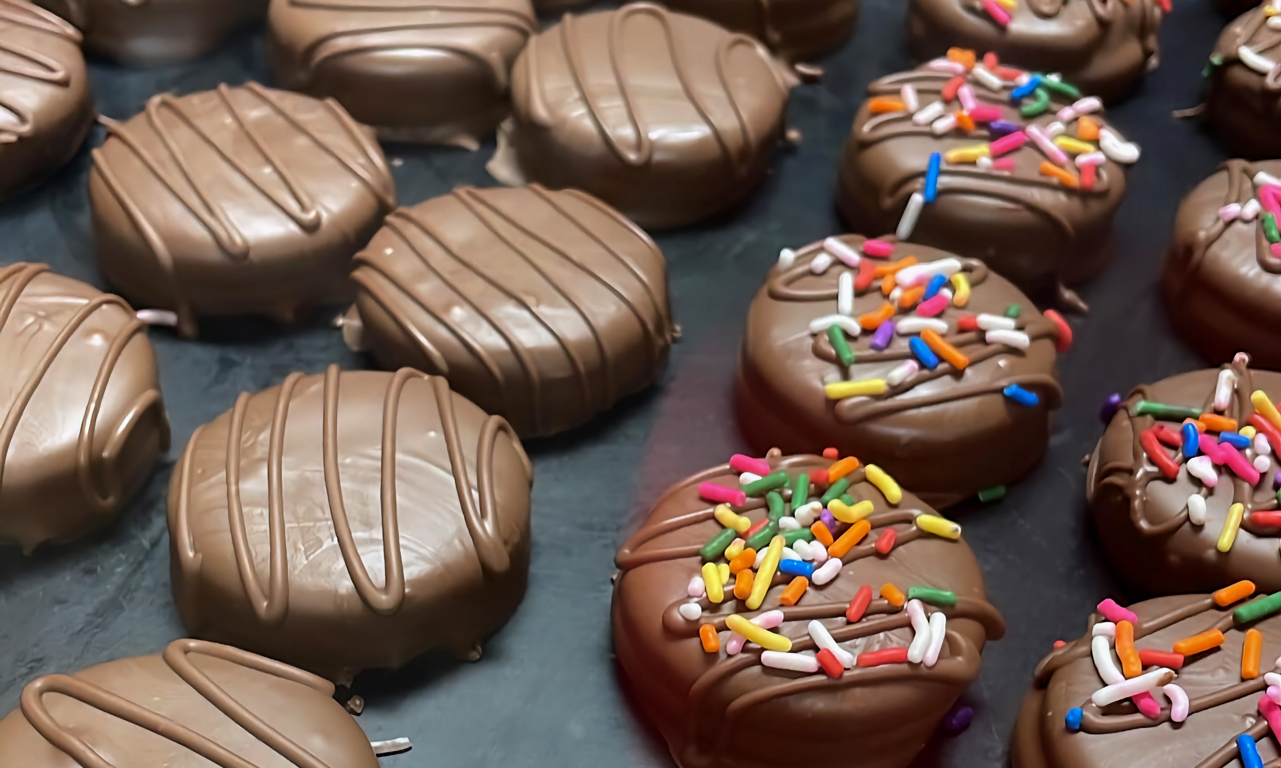 Chocolate-dipped cookies, some with rainbow sprinkles, lined up after the fryer