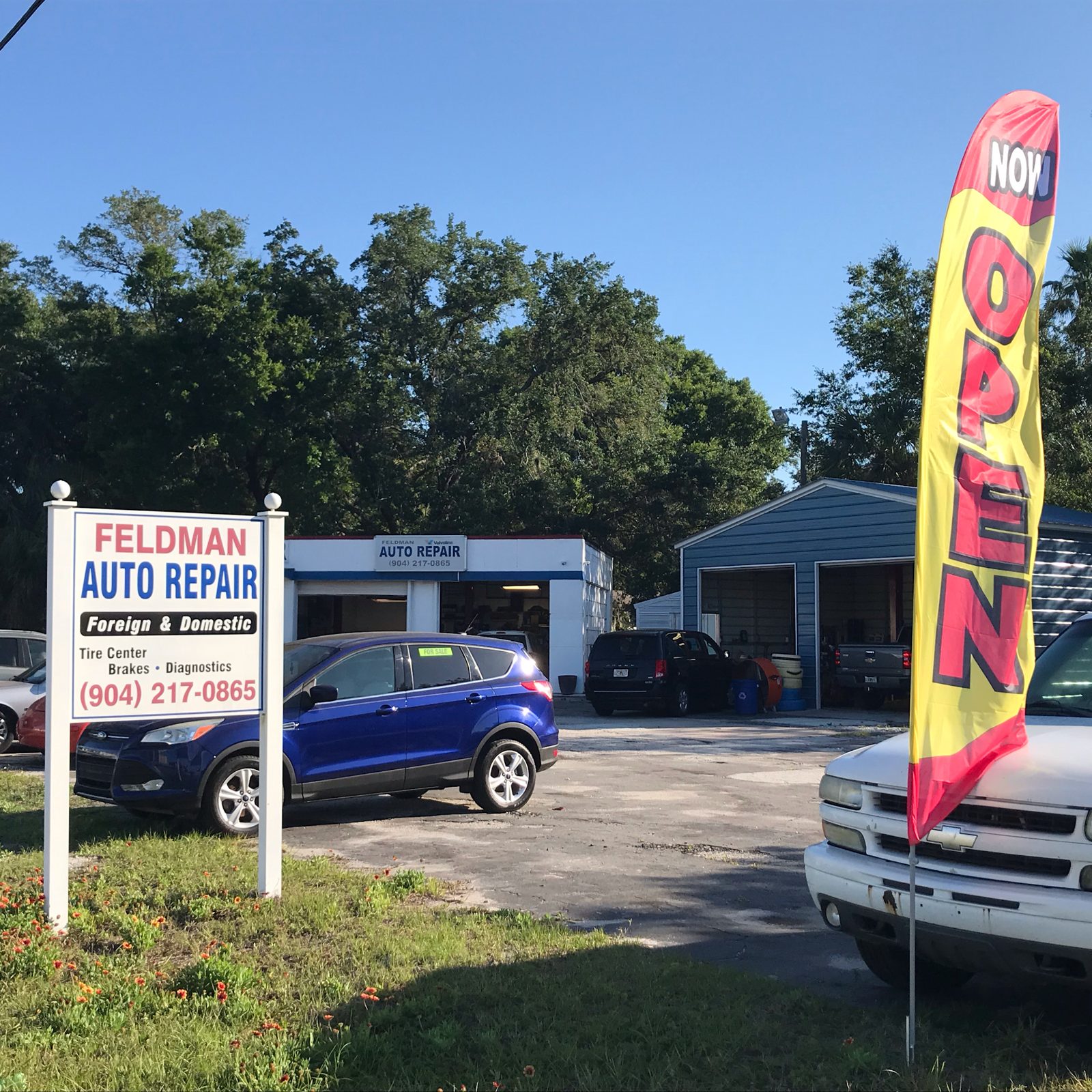 Our Feldman Auto Repair sign, white shop, and blue metal bays on North Ponce
