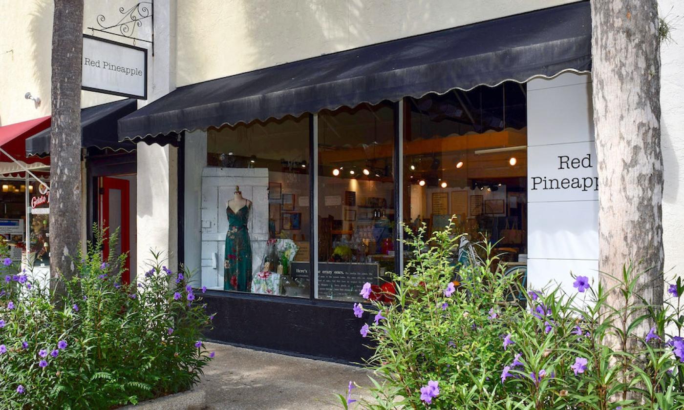 Our black scalloped awning and hanging Red Pineapple sign on St. George Street, with a floral dress in the window