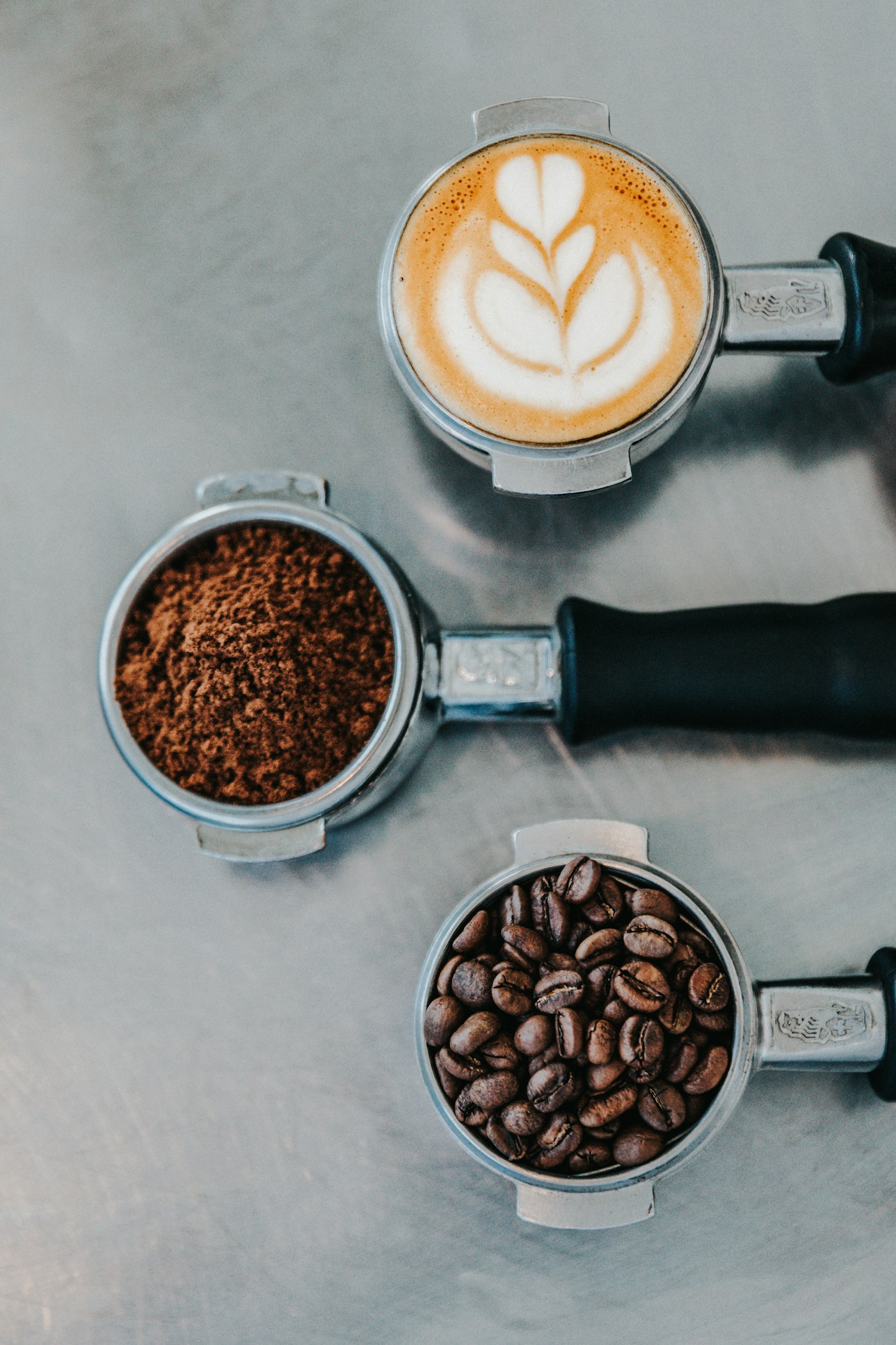 Espresso portafilters with beans, grounds, and a finished latte
