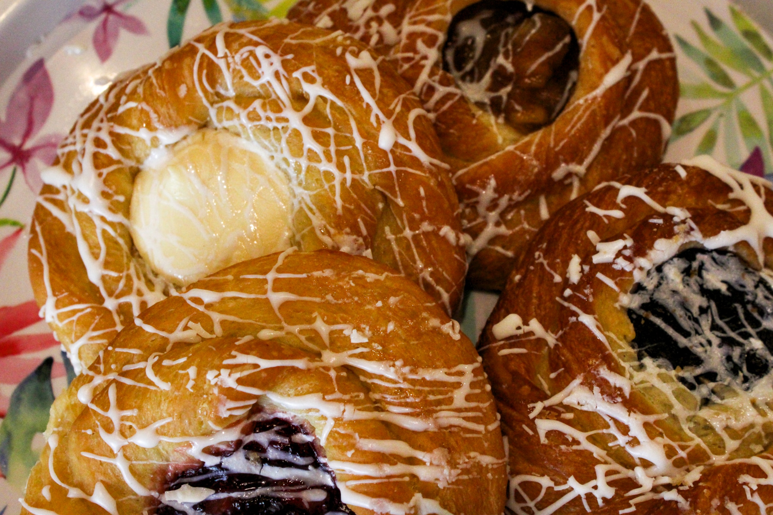 Four iced danish pastries on a floral plate, ready at our counter.