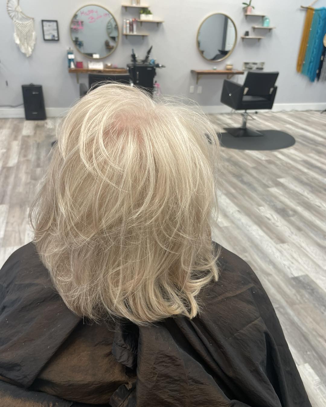 An ash blonde lob in our cape, gold mirrors behind the chair.