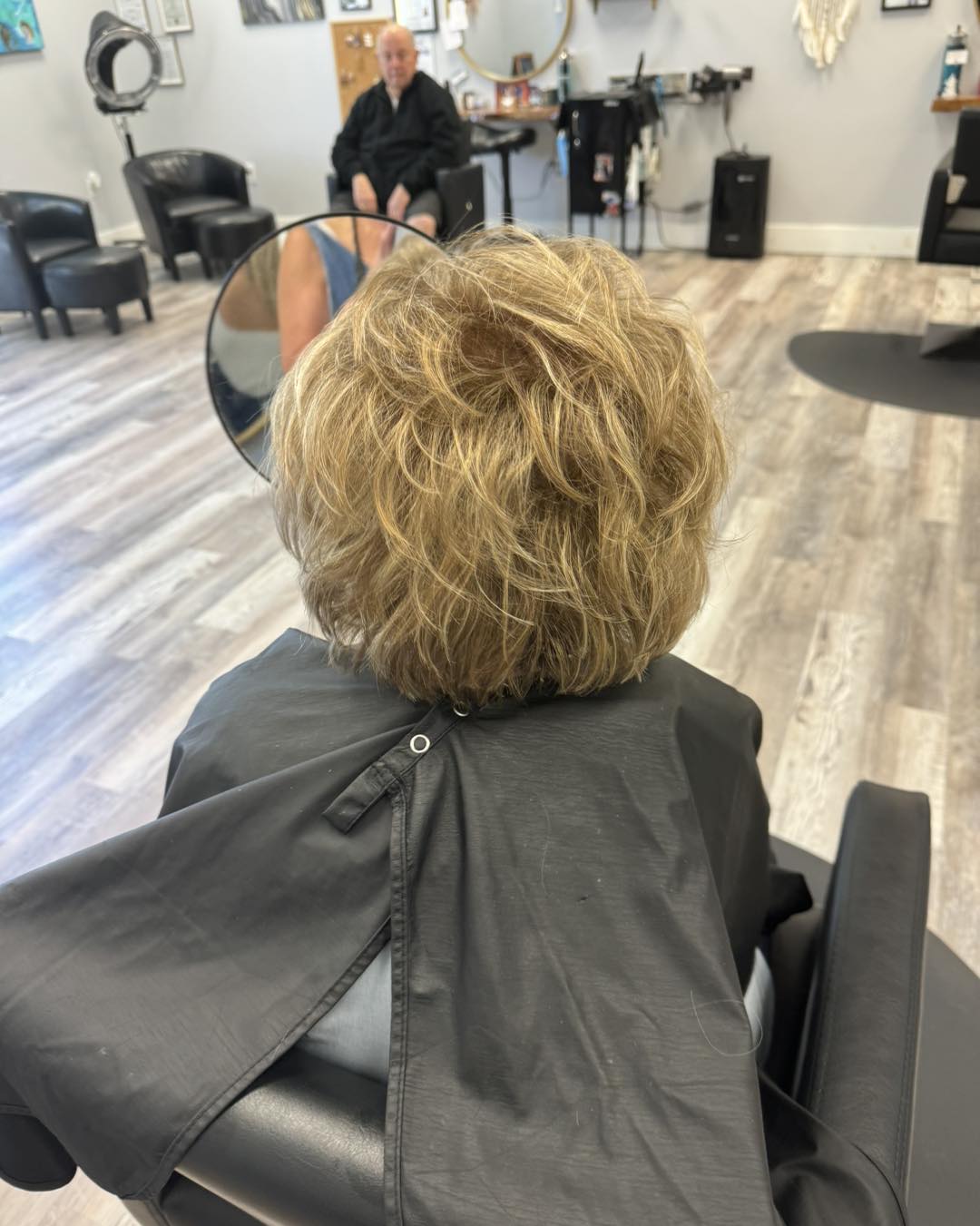 Layered honey blonde in the chair, hooded dryer and waiting seats behind us.