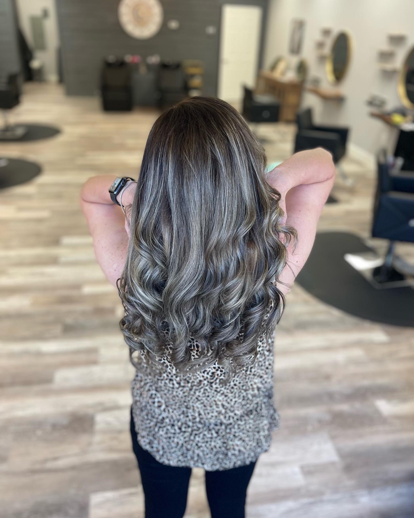 Ash blonde curls in front of our gold round mirrors and shampoo bowls.