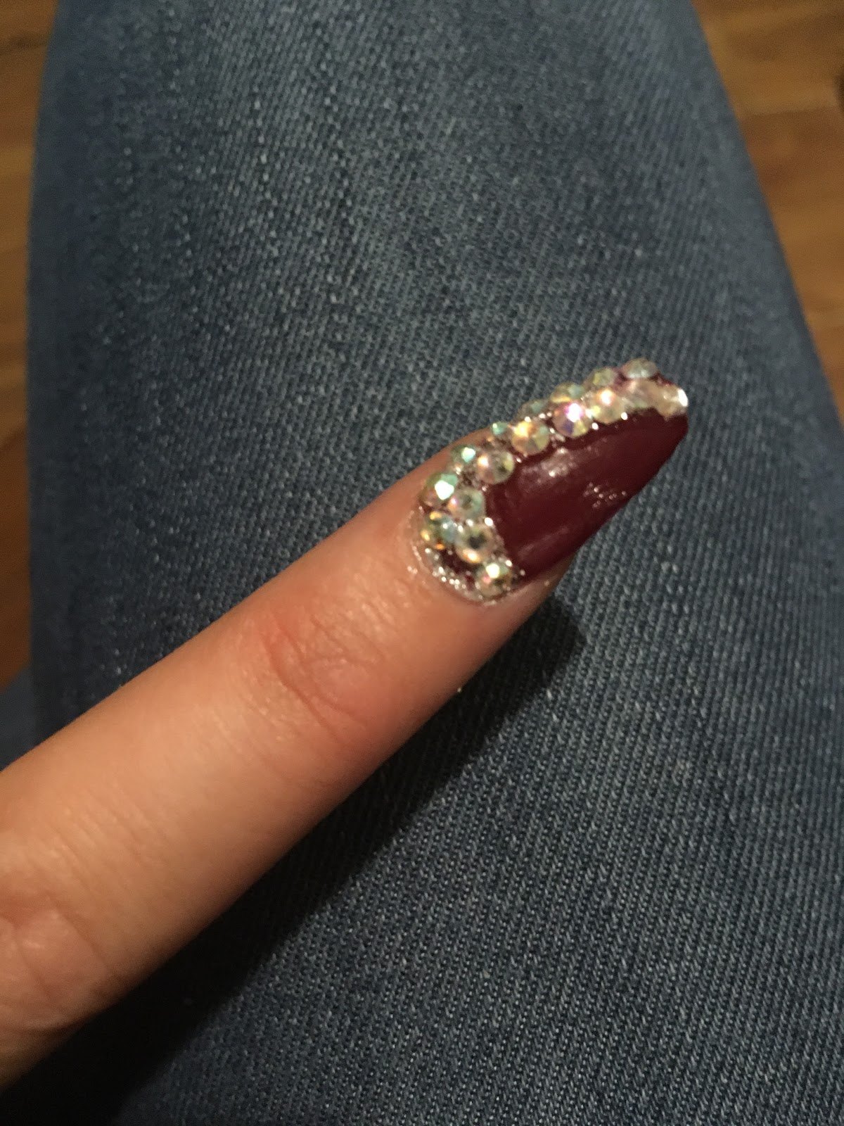 Burgundy almond nail with a rhinestone border.