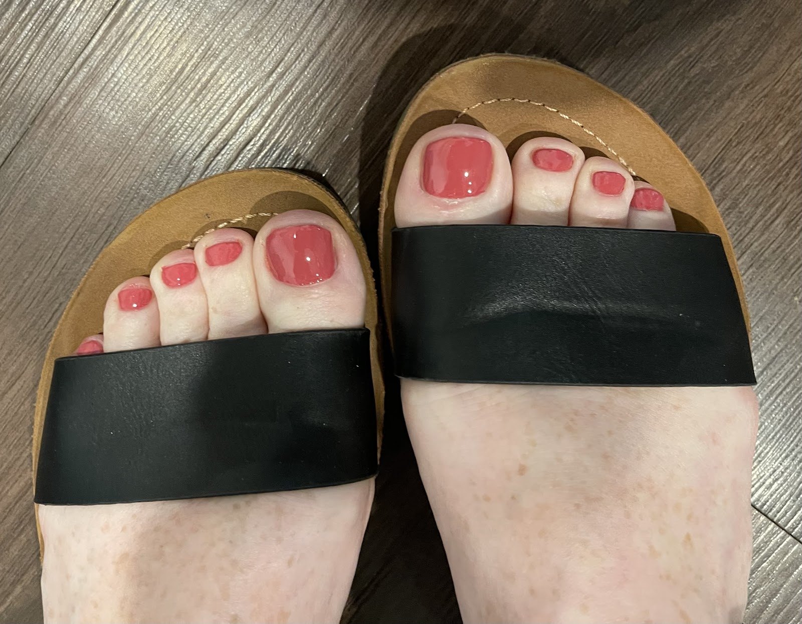 Coral gel pedicure on black slide sandals.