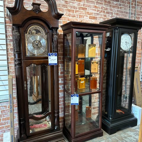 Grandfather clocks and a wood cabinet against the brick.