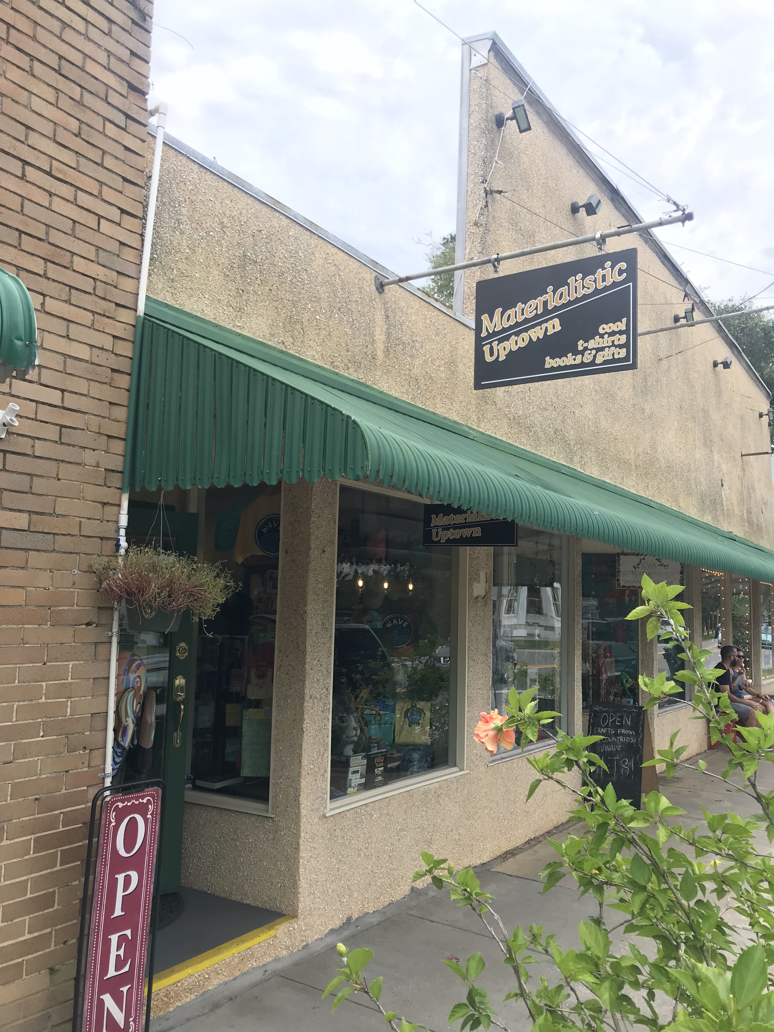 Our San Marco storefront, green awning, and Materialistic Uptown hanging sign.