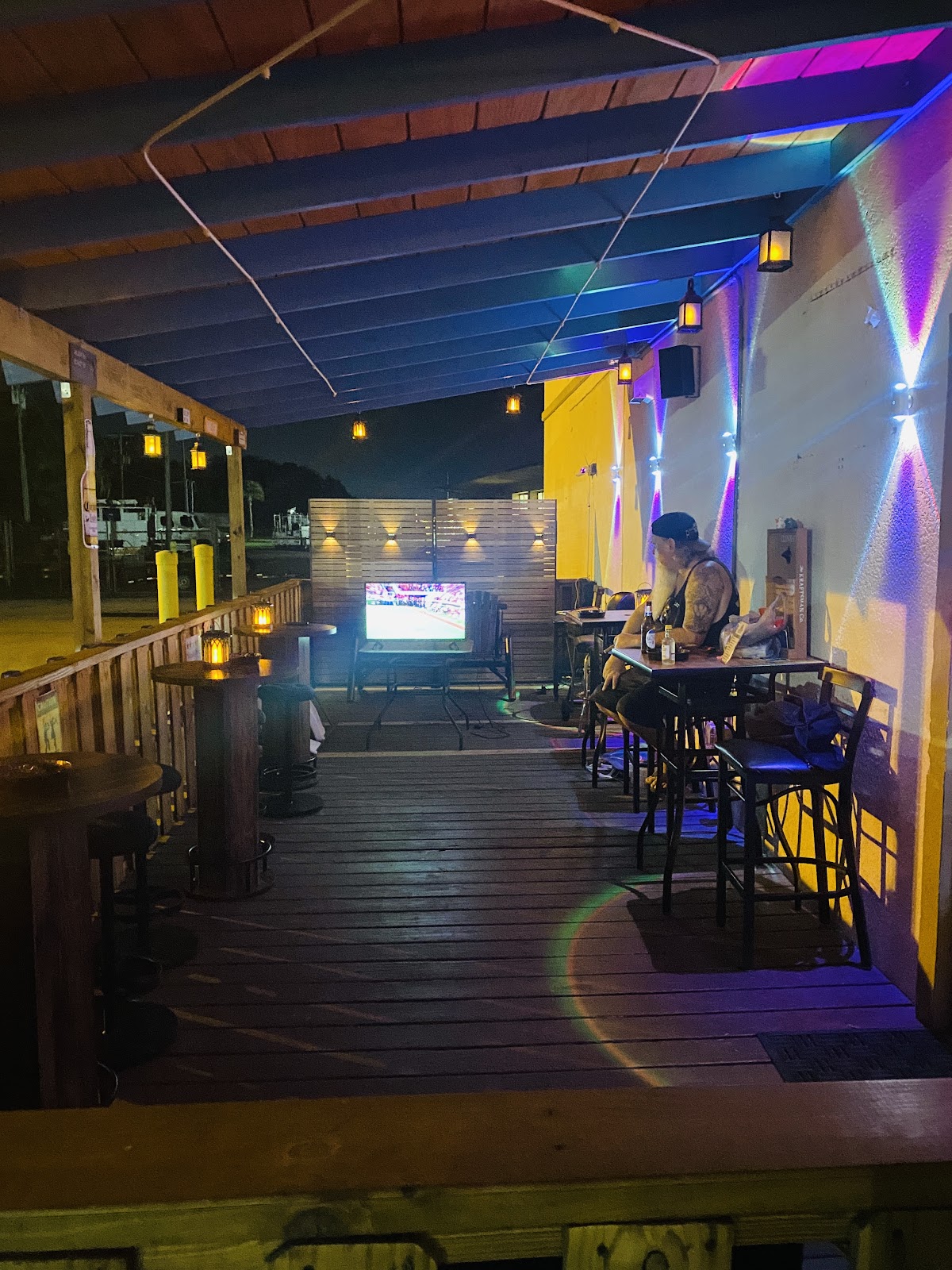Our covered wood patio at night, lanterns on the tables and a TV at the far end.