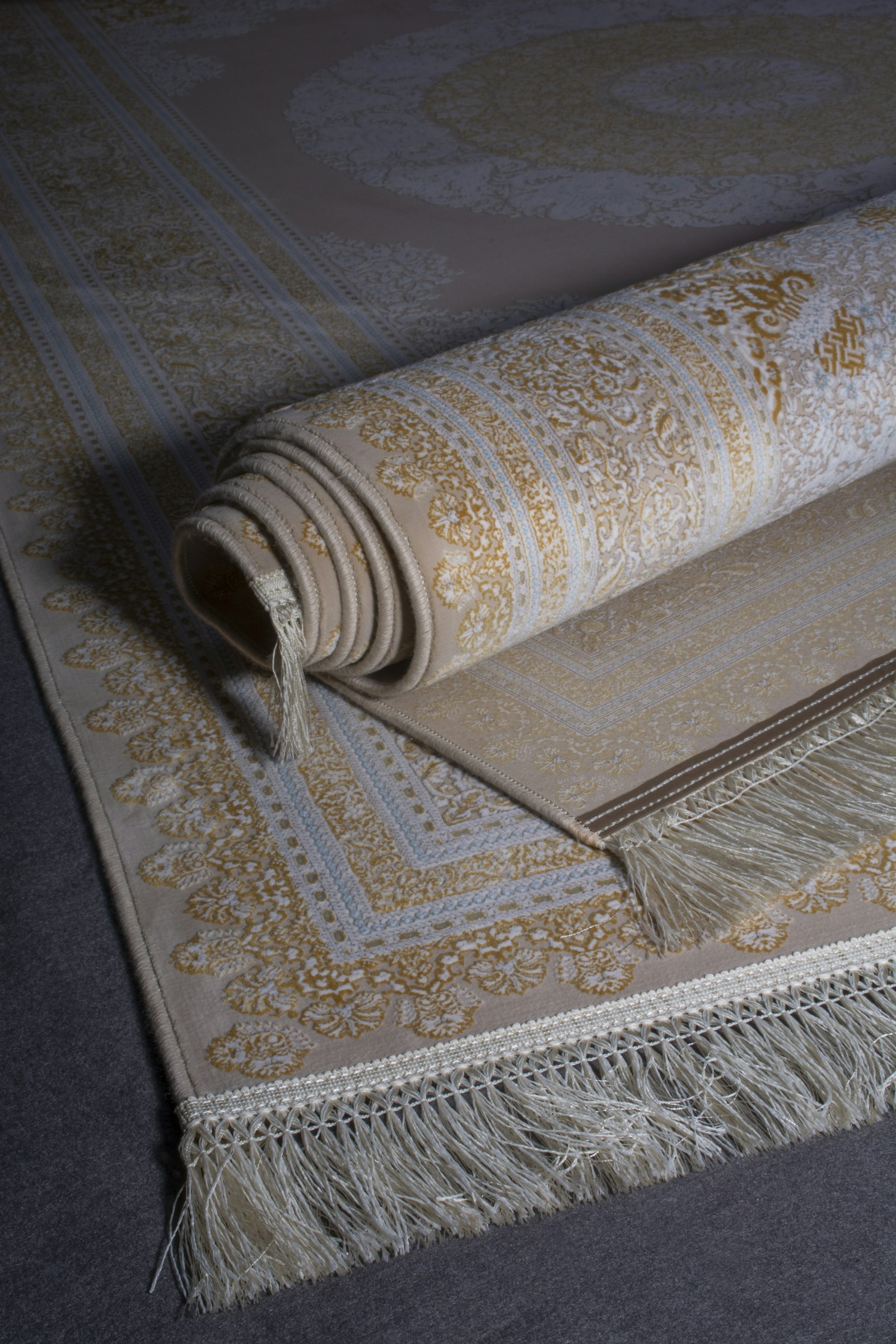 Rolled patterned rugs with cream fringe on a dark floor.