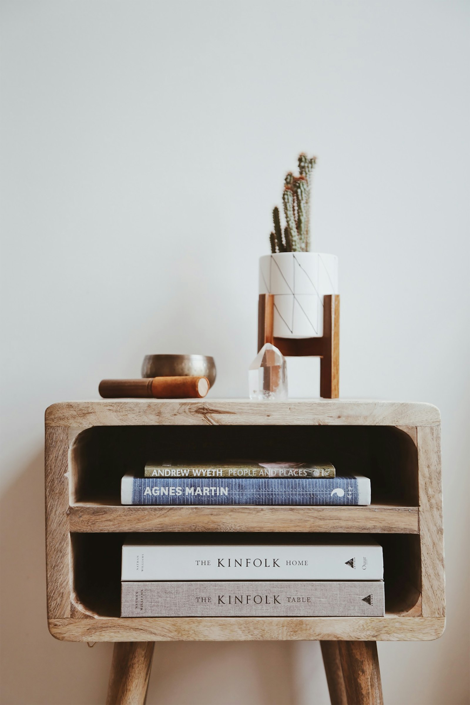 A light wood side table stacked with books and a small plant.