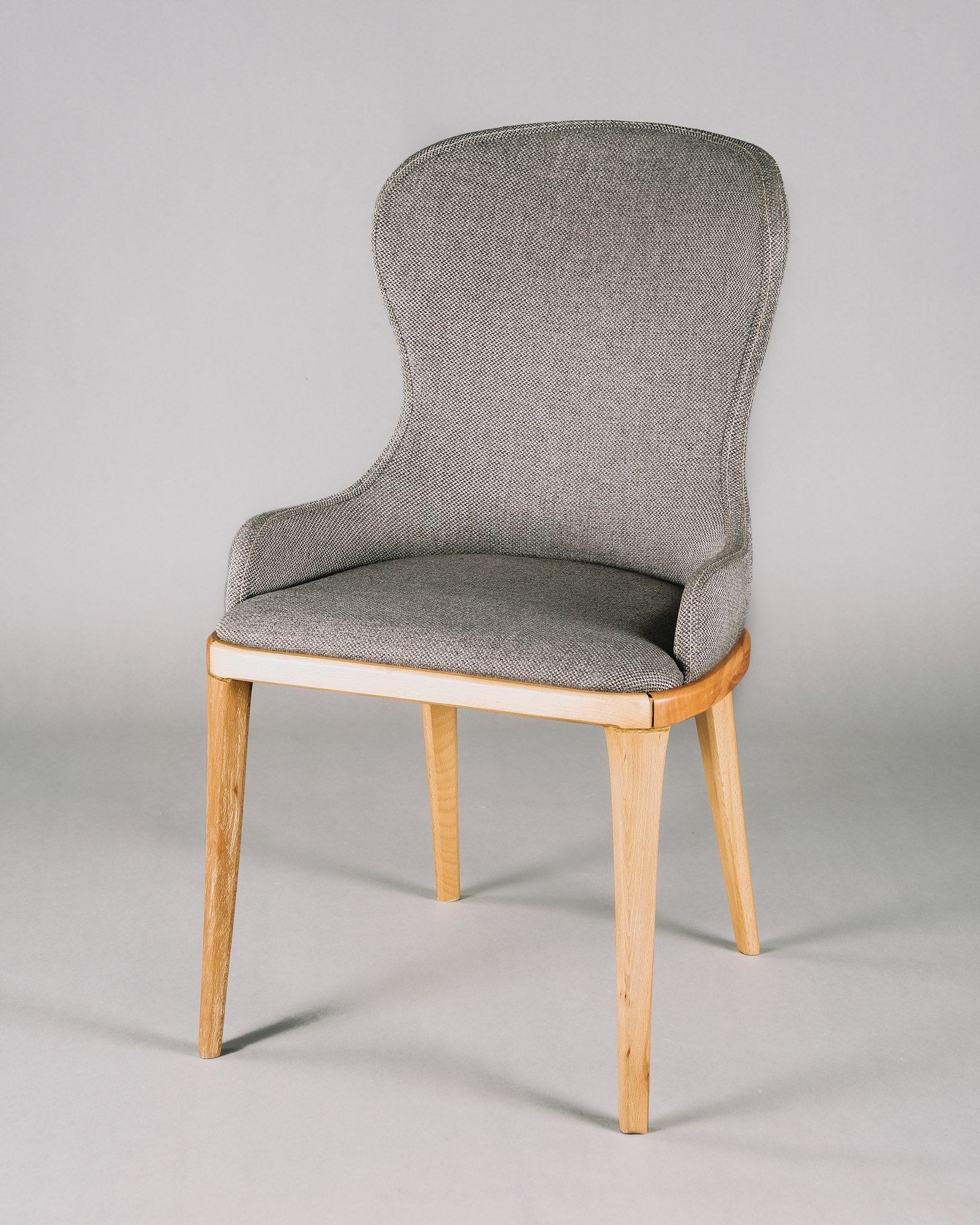 A gray upholstered chair on light wood legs.