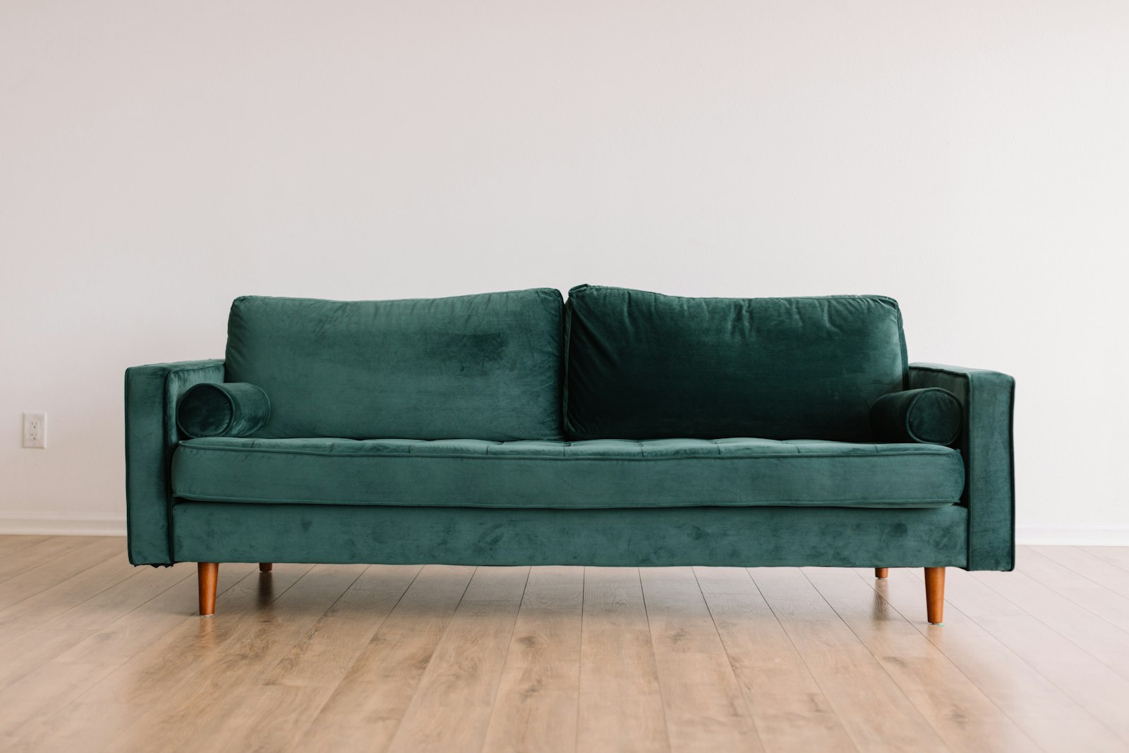 A green velvet sofa on a wood floor.