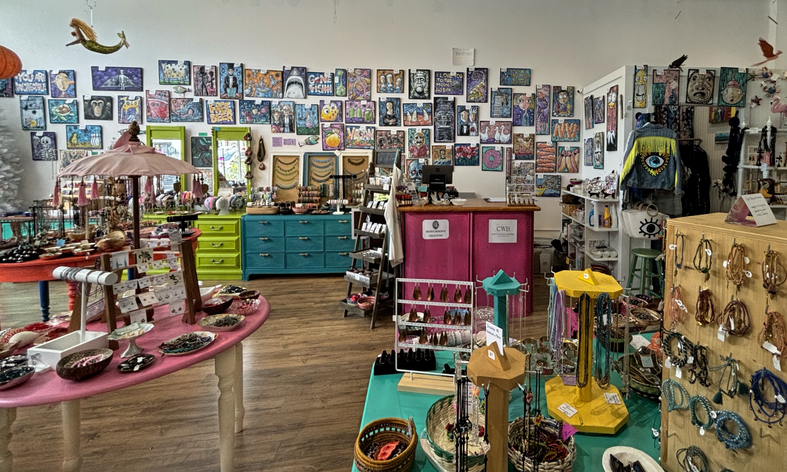 Our pink counter, jewelry bowls, and wall of handmade paintings inside Crafts Without Borders