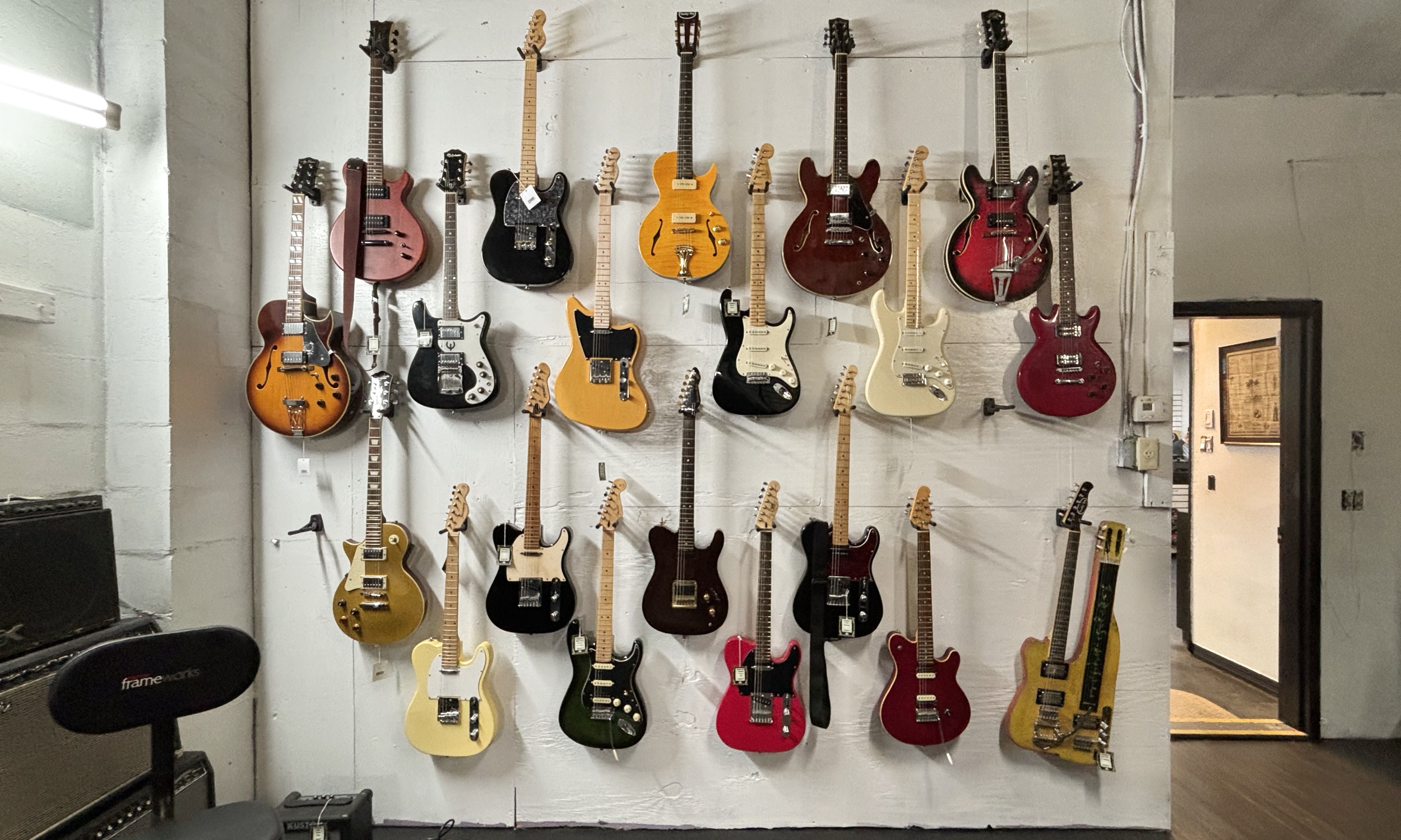 Electric guitars hanging in rows on our wall, amps stacked to the side.
