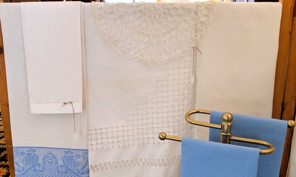 White lace and blue-border linens on our rack, with a brass towel bar holding folded blue cloth.
