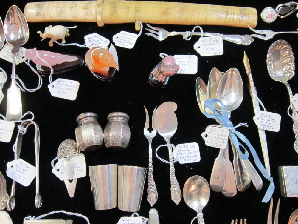 Sterling spoons, tongs, and small pieces tagged on black velvet.