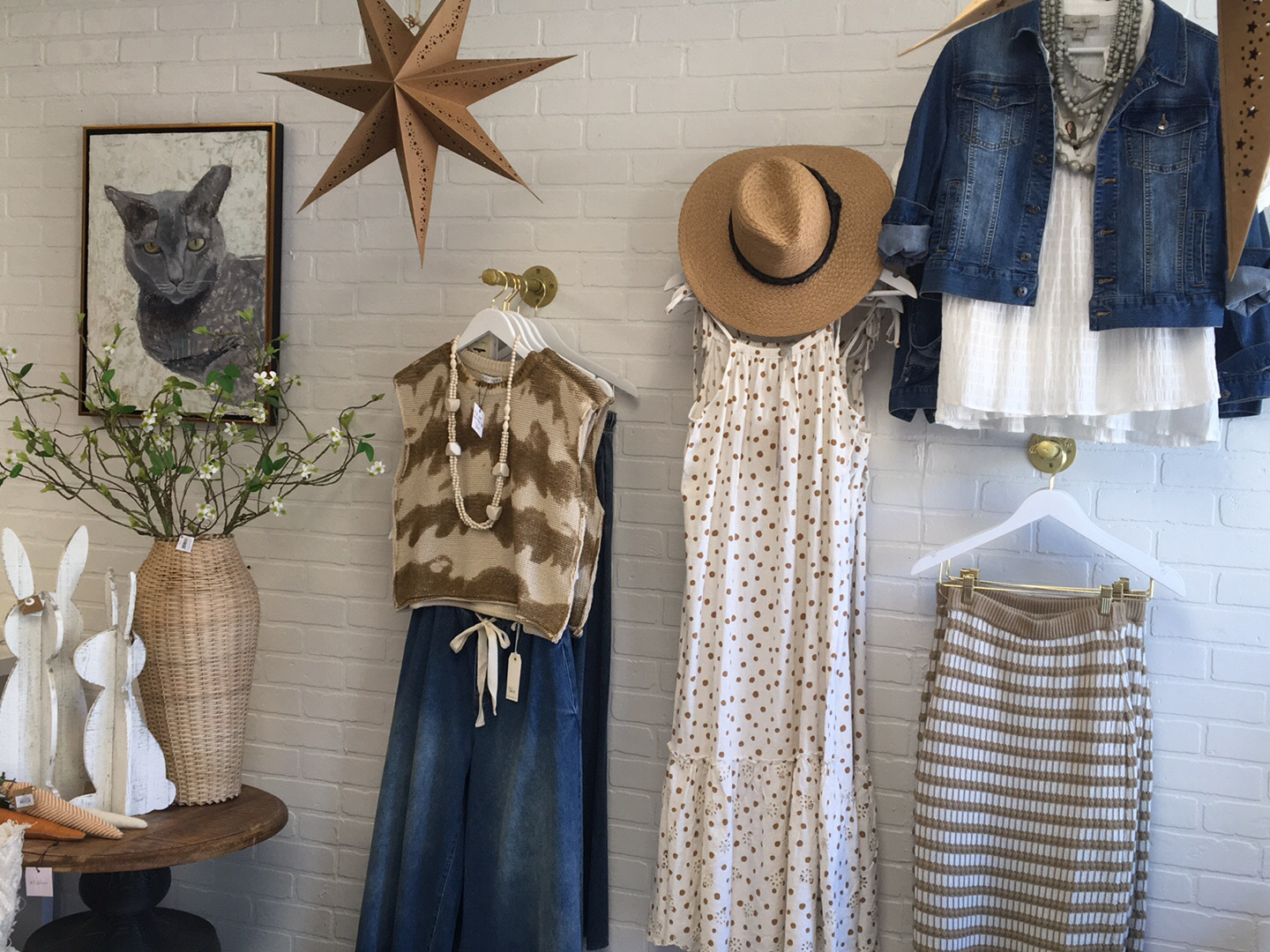 Three outfits on gold hooks, straw hat, white brick wall.