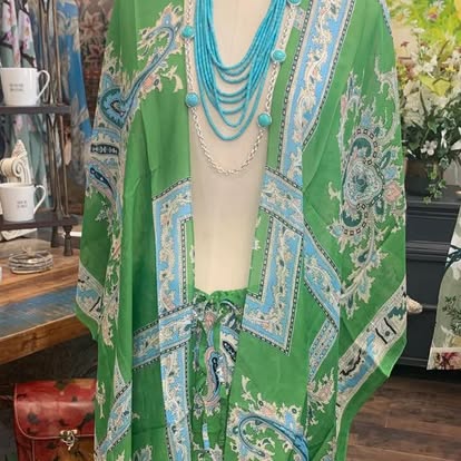 A green patterned wrap on a mannequin with turquoise beads.
